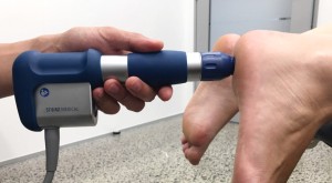 Demonstration of a shockwave device being used on the sole of a persons foot.