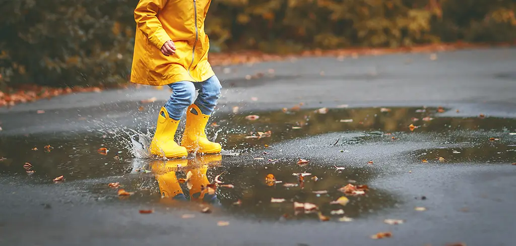 A child in a raincoat and gumboots splashes in a puddle